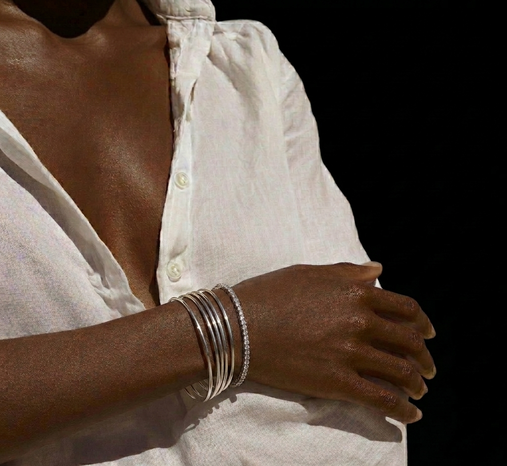Person wearing multiple silver bracelets on a white shirt against a black background